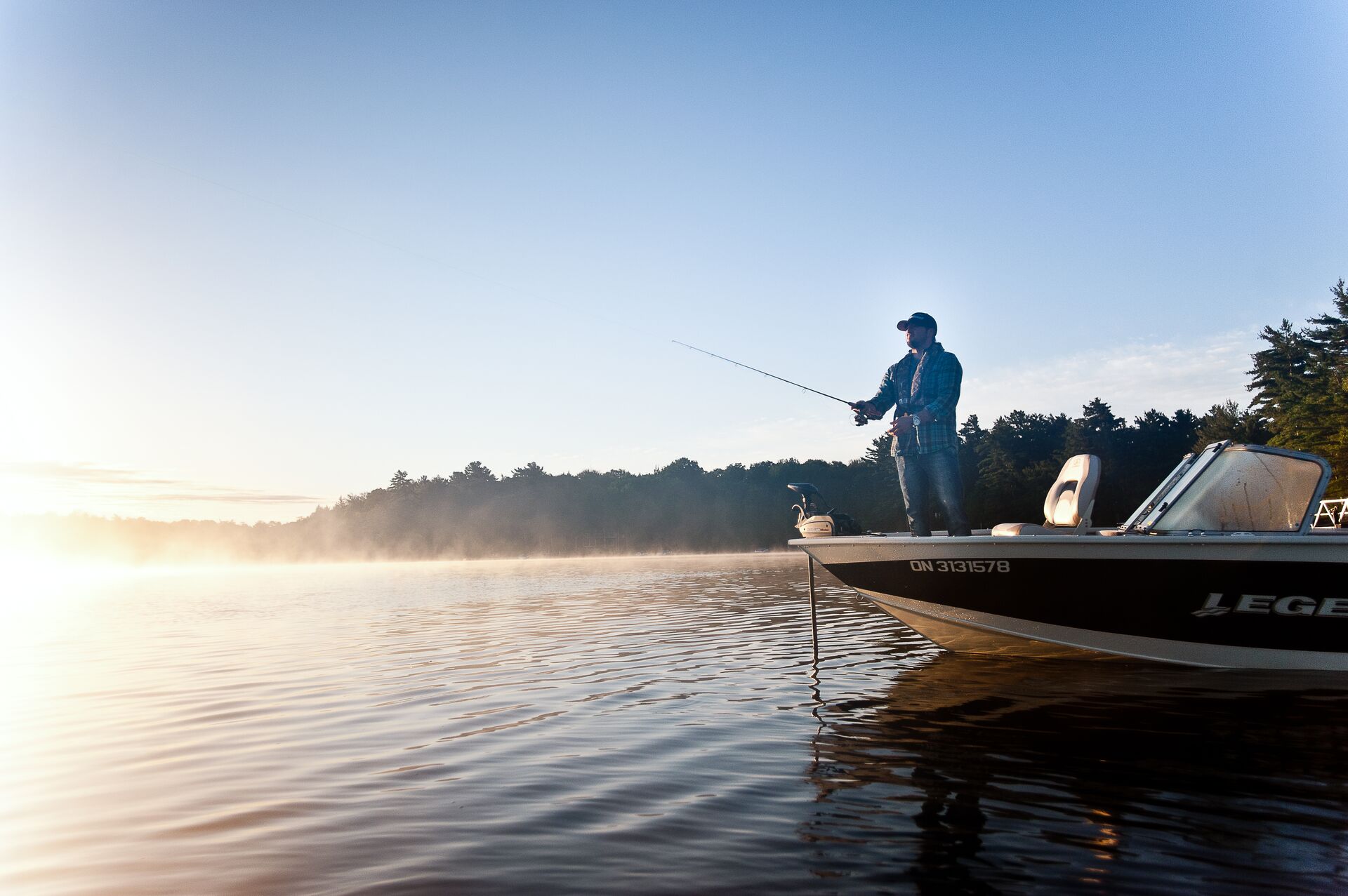 A man at the front of a fishing boat holding a rod and reel over the water. 