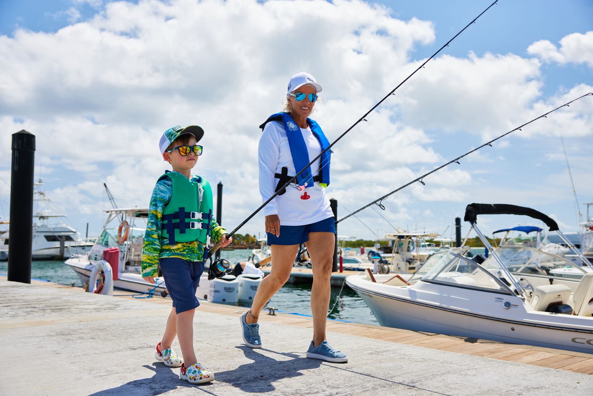 A boy and a woman holding fishing rods walk on the dock, fishing boats concept. 